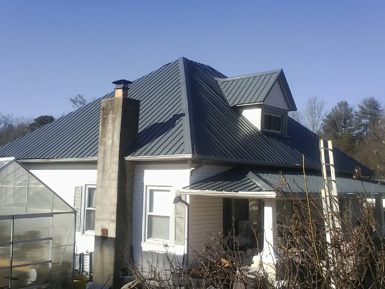 Dark blue standing seam metal roof on a white farmhouse with dormer — Slate & Tile Roof Repair by Roofing Brothers in Keene Valley
