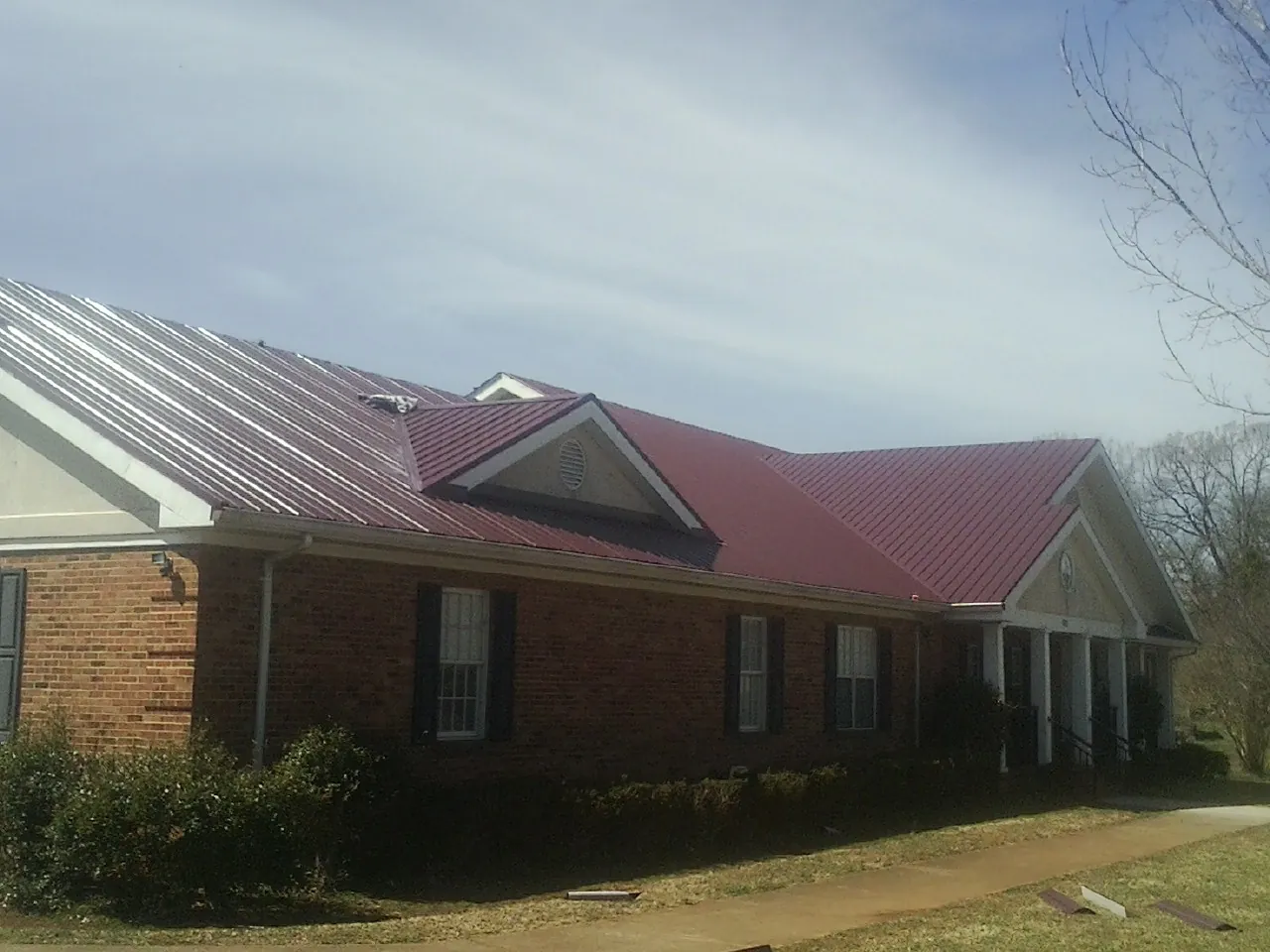 Red metal roof with gabled entries on a long brick building, from a Hail Damage Roof Repair job in Keene Valley