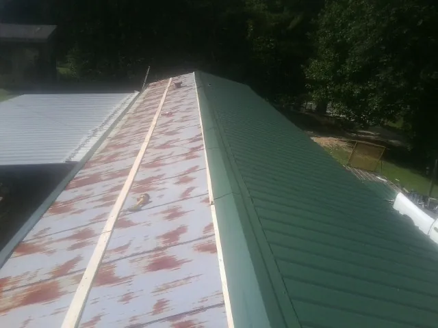 Old rusted panels beside newly installed green metal roofing — Wind Damage Roof Repair by Roofing Brothers in Keene Valley