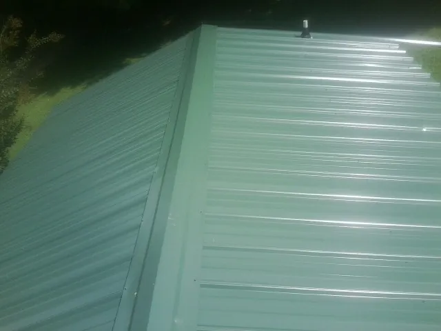 New green metal panels meeting at the ridge of a roof — Flat Roof Repair work by our crew in Keene Valley