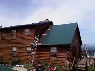Green metal roof going on a two story log home with ladders set in Keene Valley