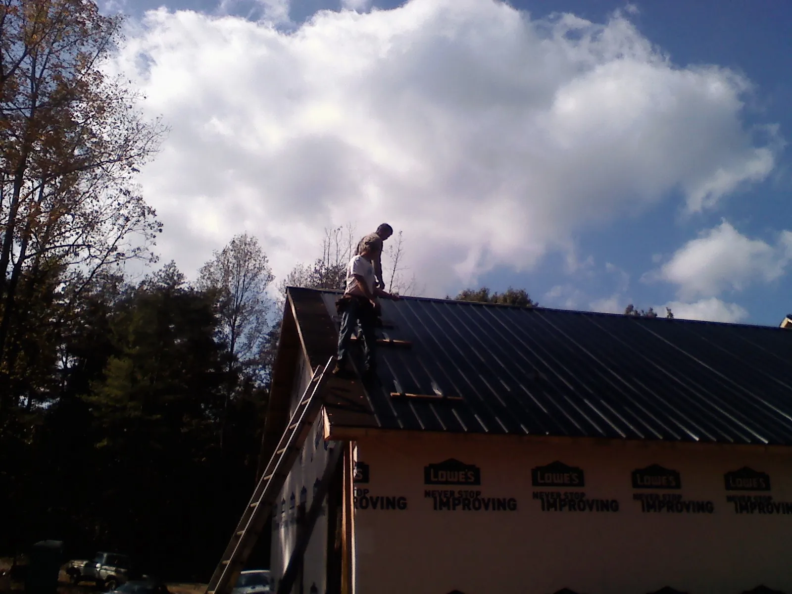 Roofer fastening dark metal panels high against a cloudy sky, from a Roof Inspection job in Keene Valley