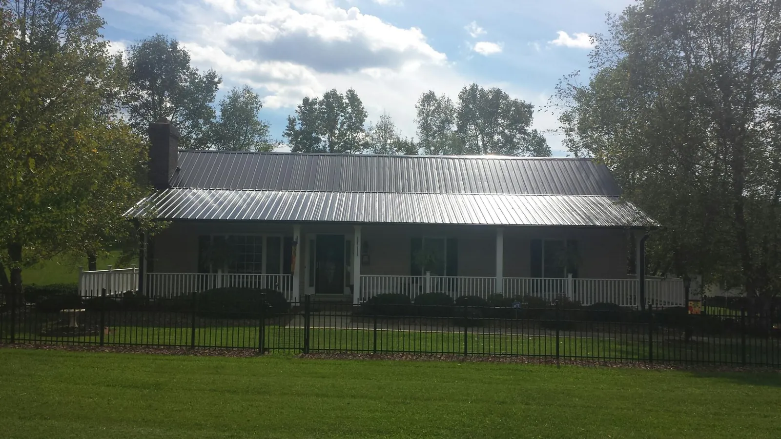 Gray metal roof on a brick ranch with a full width front porch — Gutter Guard Installation work by our crew in Keene Valley