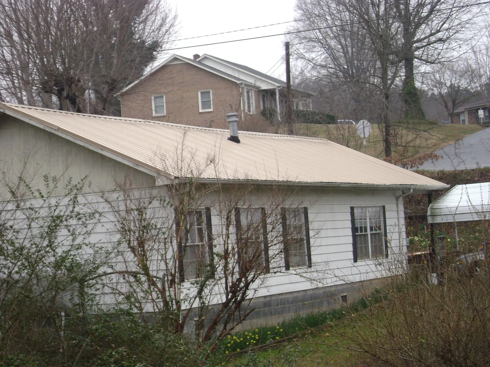 Tan metal roof on a white sided house set into a hillside — Commercial Roofing by Roofing Brothers in Keene Valley