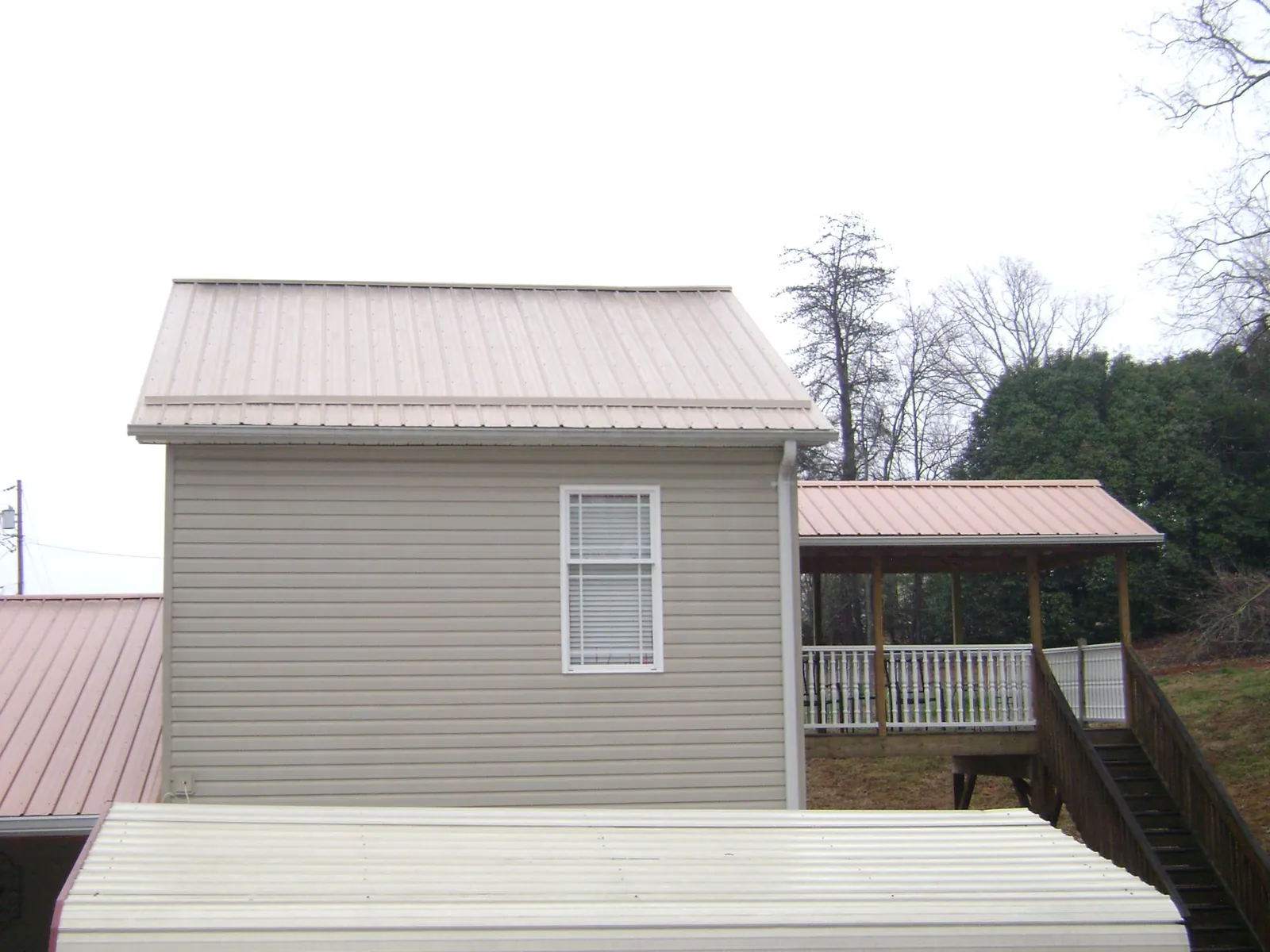 Tan metal roofs on a two story addition and attached porch, from a Roof Replacement job in Keene Valley